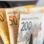 A imagem mostra cédulas de dinheiro brasileiro em close, com notas de R$ 20, R$ 50 e R$ 200 posicionadas lado a lado
