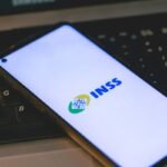 Aplicativo do INSS aberto na tela de um smartphone sobre um teclado de computador, representando serviços previdenciários, benefícios e processos contra o INSS.