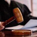 Martelo de juiz sobre uma mesa durante sessão judicial, com documentos ao fundo, representando decisões judiciais, processos e atuação da Justiça.